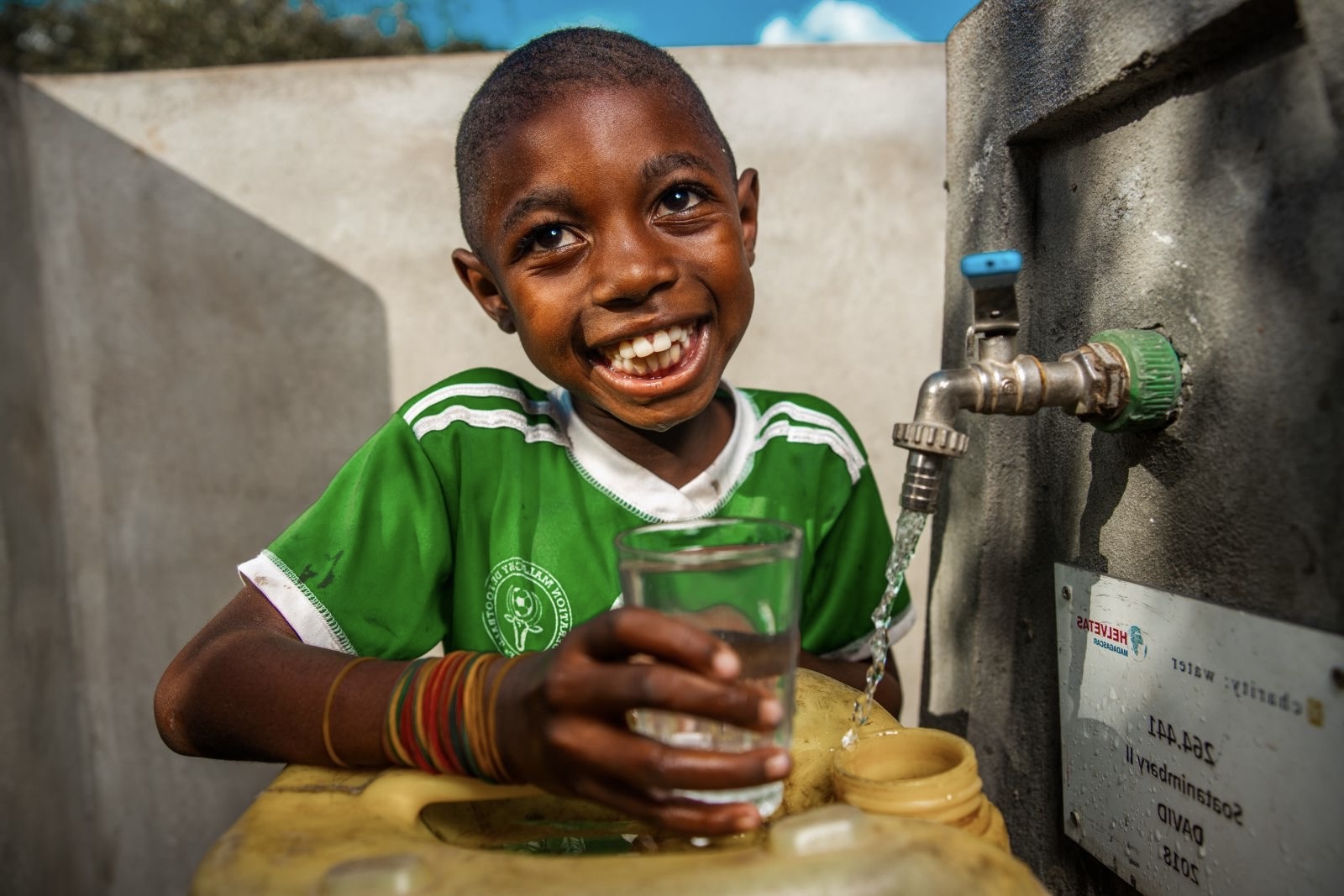 Child smiling with a glass of clean water at a tap